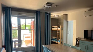 Une pièce avec une table en bois, des chaises bleues, un lit superposé et une porte-fenêtre coulissante donnant sur un espace extérieur.