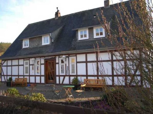 Ein traditionelles Fachwerkhäuschen mit geneigtem Dach, zwei Fenstern im Obergeschoss und einer Holztür.