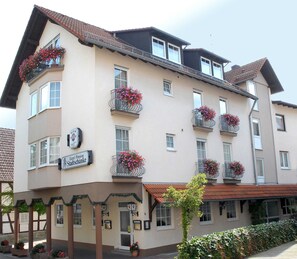 Un hotel de varios pisos con balcones decorados con macetas de flores, un cartel que indica que es una pensión y un estilo arquitectónico tradicional.