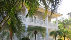Un edificio de dos pisos con fachada blanca, un balcón en el nivel superior y una pequeña escalera que lleva a la entrada.