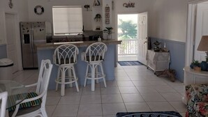 Una cocina con refrigerador, un comedor con mesa y sillas, y un balcón con vista a la vegetación.