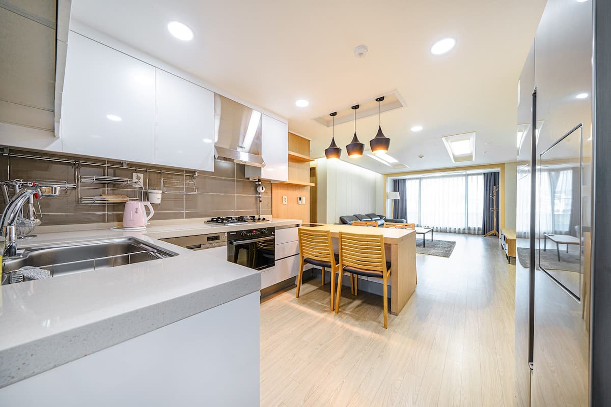 Une cuisine moderne dotée d’un îlot central, d’appareils électroménagers en acier inoxydable et de luminaires suspendus.