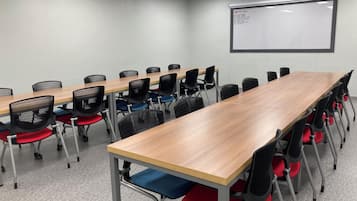 A conference room with a long table, multiple chairs, a whiteboard, and a projector screen.