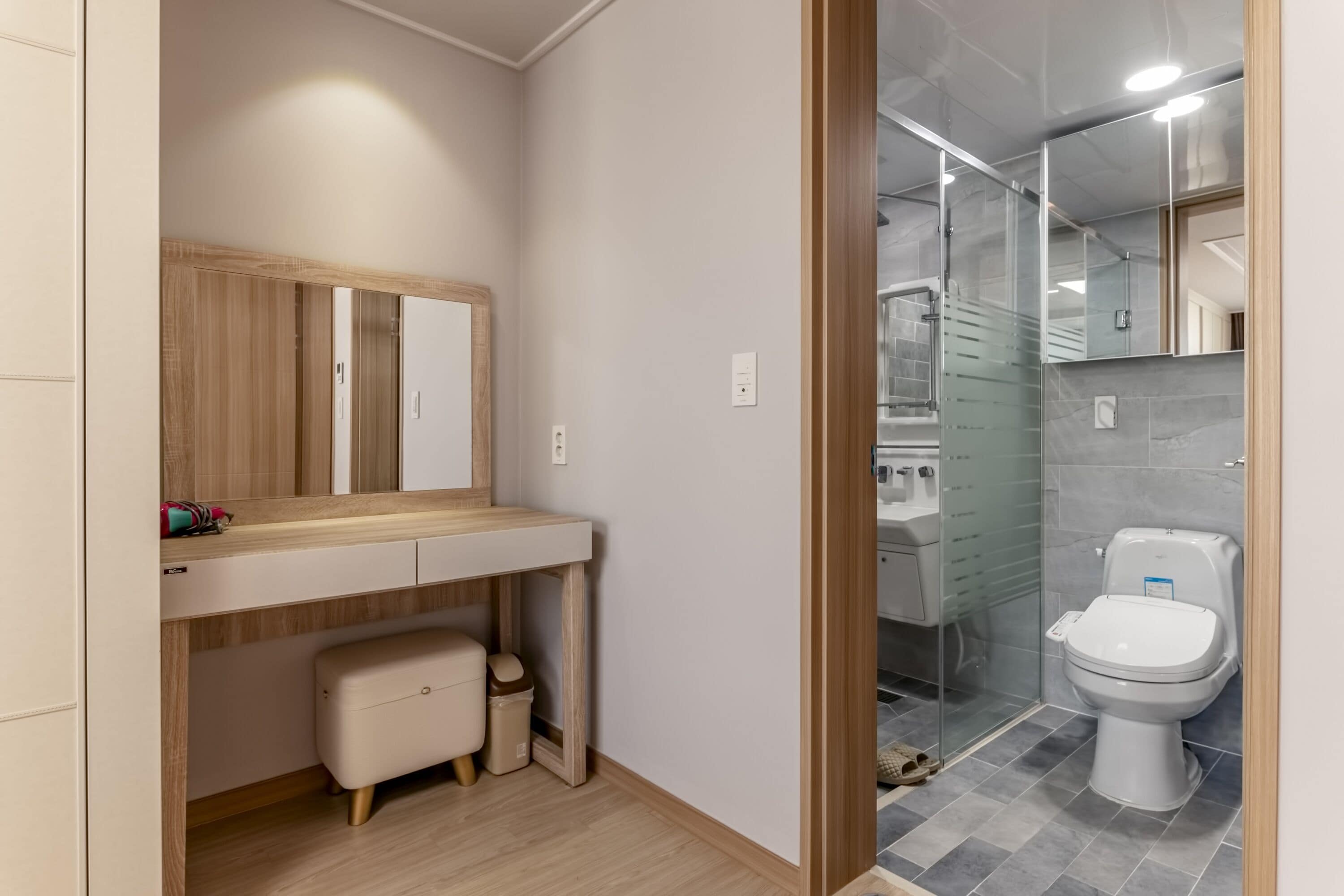 Een moderne badkamer met een houten wastafelmeubel, een spiegel, toilet en douche.