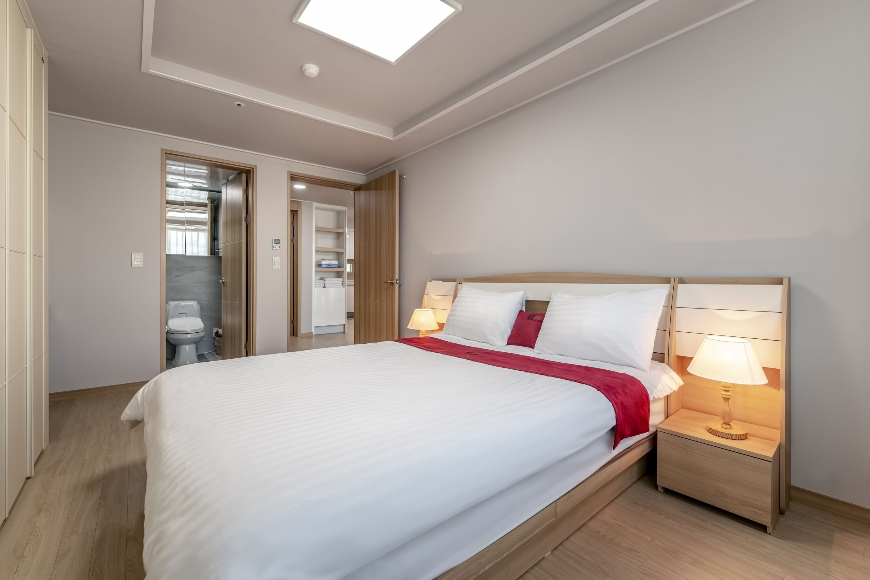 Une chambre d’hôtel moderne, dotée d’un grand lit, de lampes de chevet, d’une armoire et d’une salle de bain visible à travers une porte ouverte.
