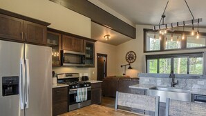 A kitchen with a stainless steel refrigerator, a microwave, a stove, and a sink. There is a wooden countertop and a hanging light fixture. - New Venture- 3BR Cabin by Terry Peak (Lead)