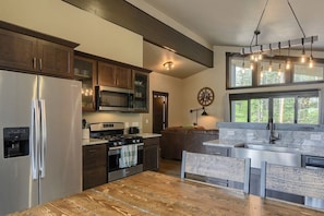 A kitchen with a stainless steel refrigerator, a microwave, a stove, and a sink. There is a wooden countertop and a hanging light fixture.