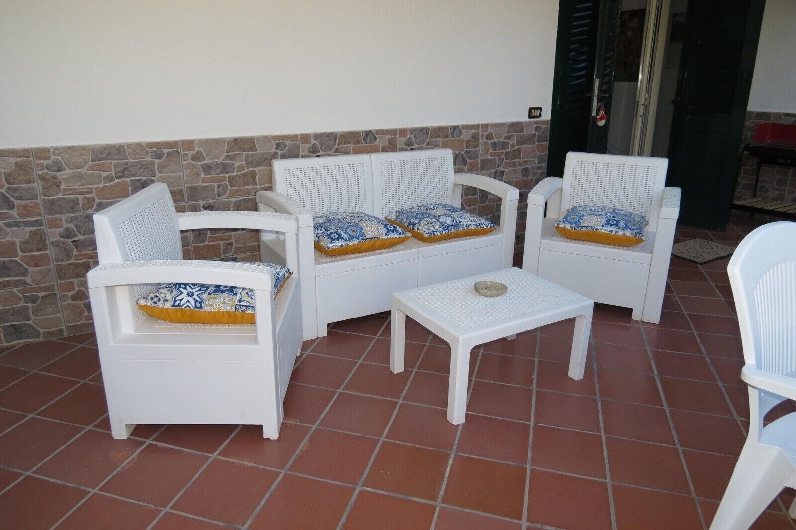 A patio area with white wicker furniture, including two chairs, a sofa, and a small table.