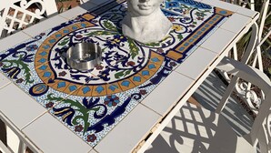 A table with a decorative tile pattern, a white metal chair, and a white vase with flowers. - 2 steps from the sea of the Gulf of Carini (Carini)