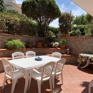 Eine Terrassengruppe im Freien mit weißem Tisch und Stühlen, umgeben von Blumentöpfen und einer Steinmauer.