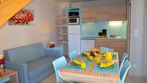 Un espace de vie compact comprenant une table à manger préparée pour le petit-déjeuner, un canapé et une kitchenette.