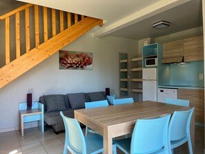 A modern kitchen with wooden cabinets, a dining table with chairs, a sofa, and a staircase.