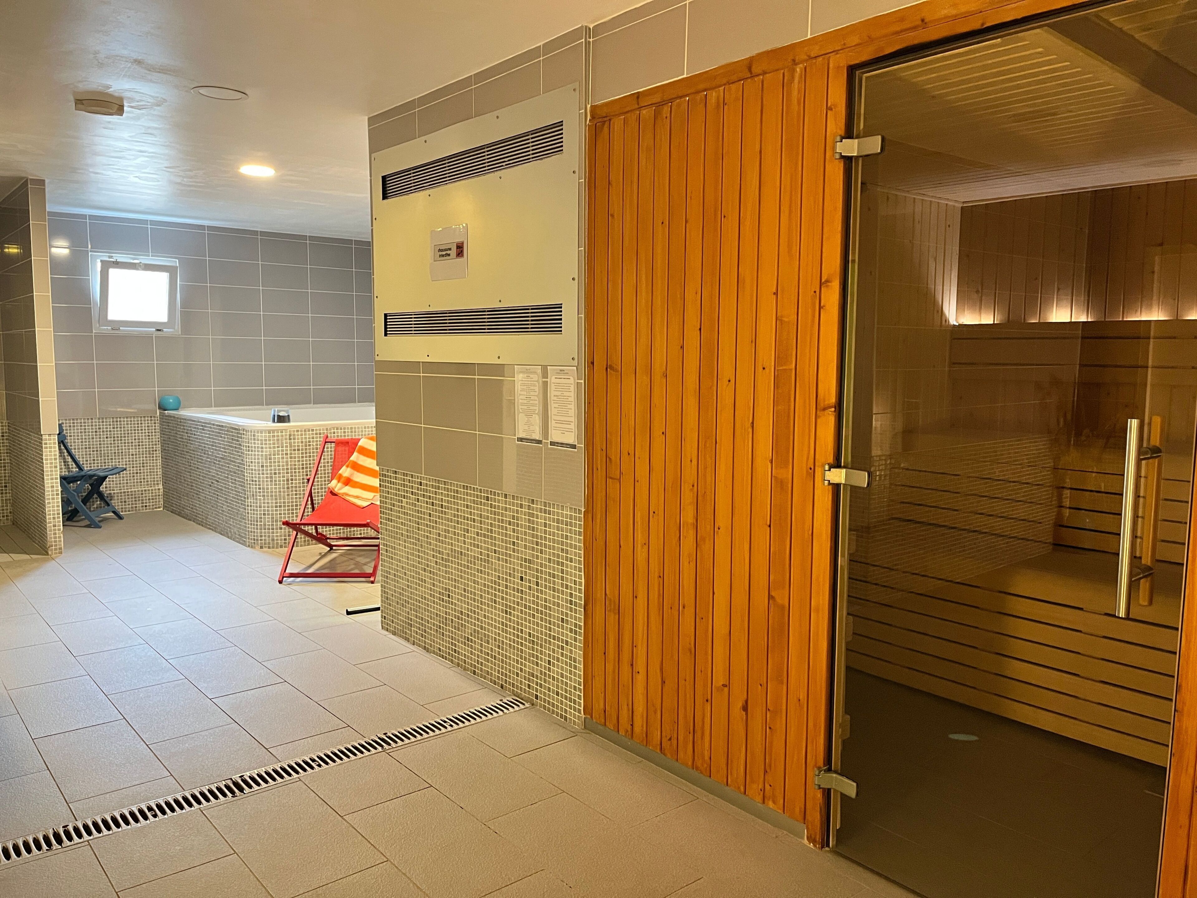 Un bany d'hotel amb una porta de fusta, parets revestides de rajoles, una zona de dutxa i una finestra.