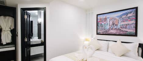 A hotel room with a bed, a painting, a bathroom, and a robe rack.