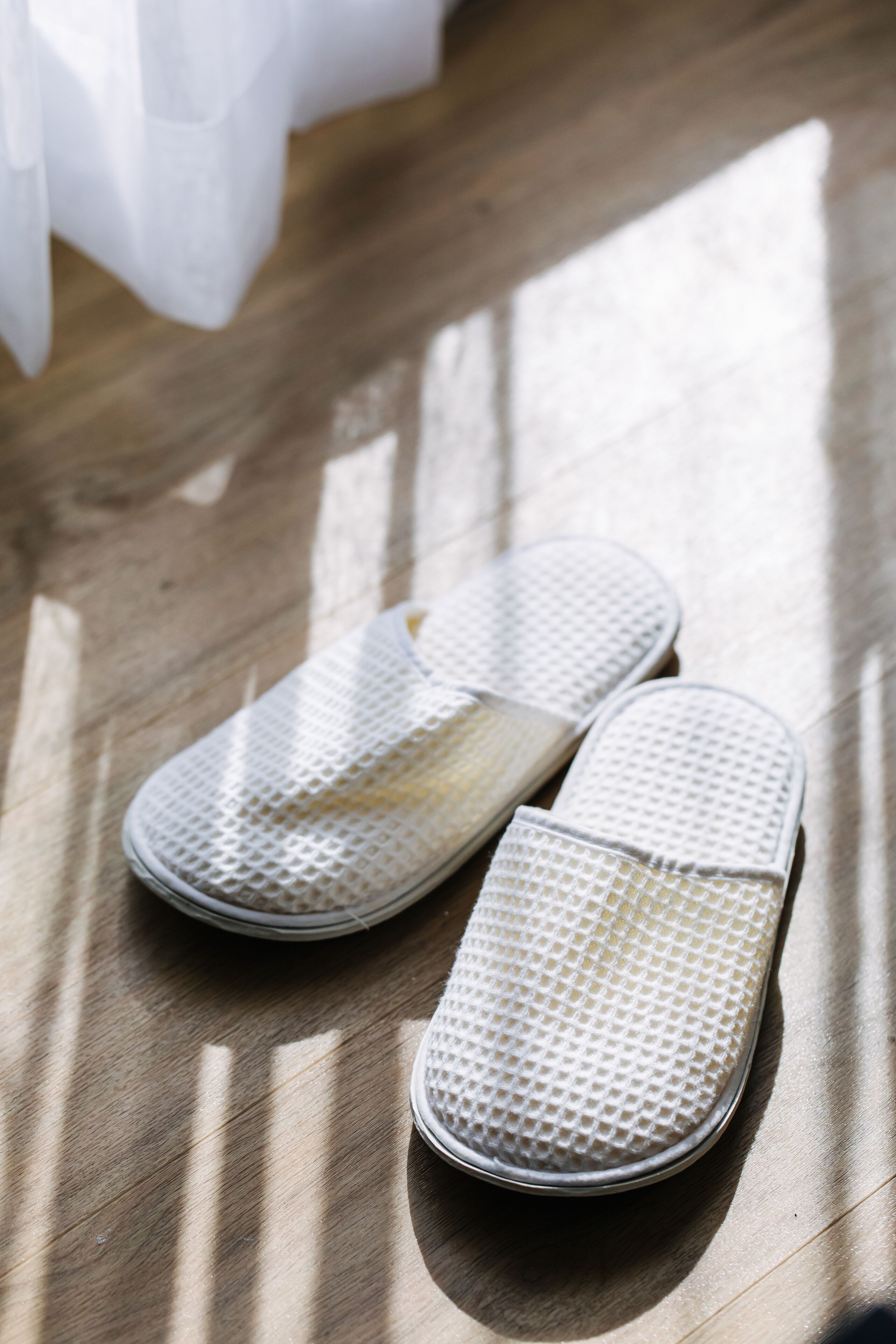 A pair of white mesh slippers on a wooden floor.