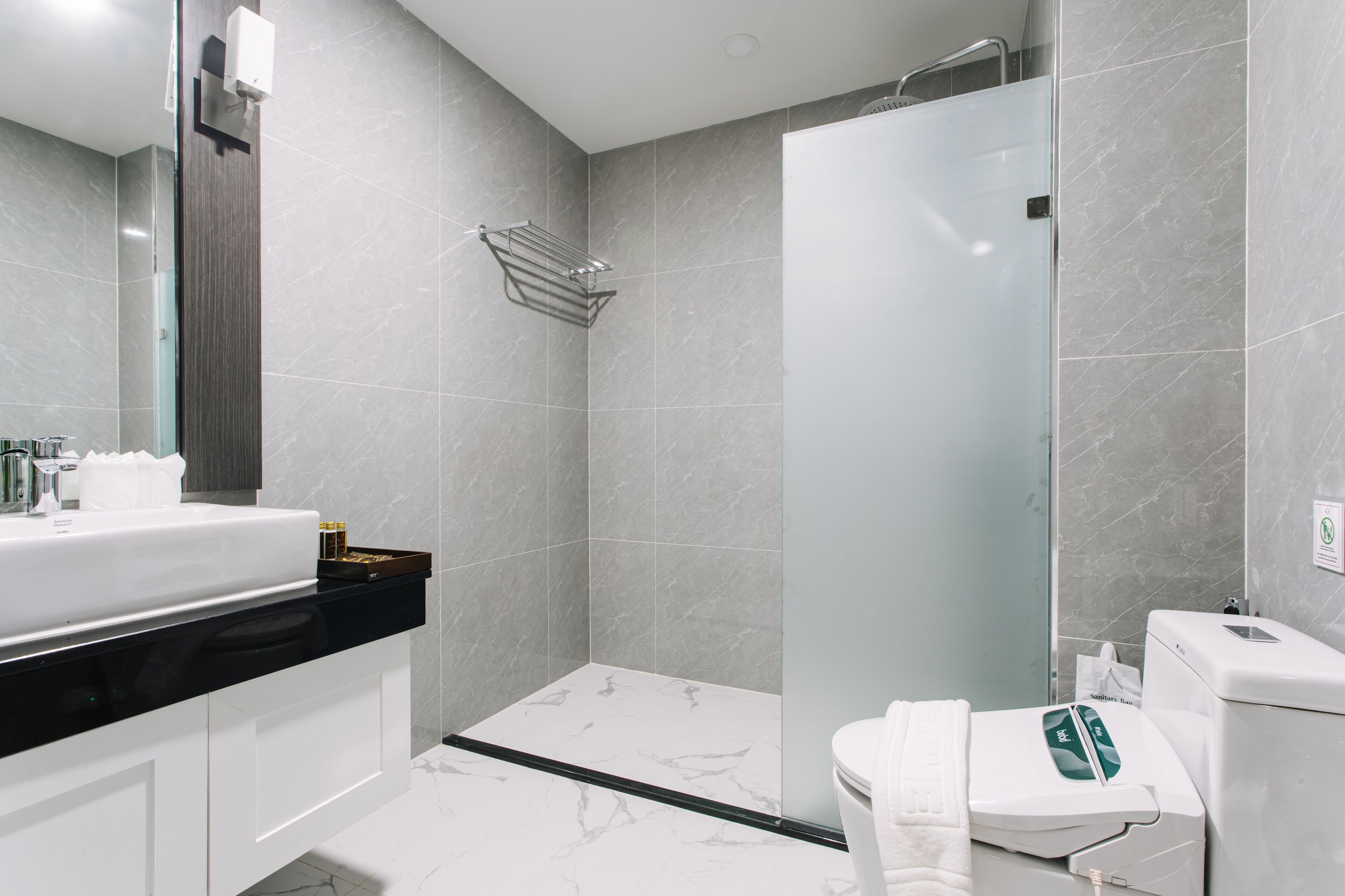 A modern bathroom with a glass-enclosed shower, a white sink with a black countertop, and a toilet with a bidet attachment.