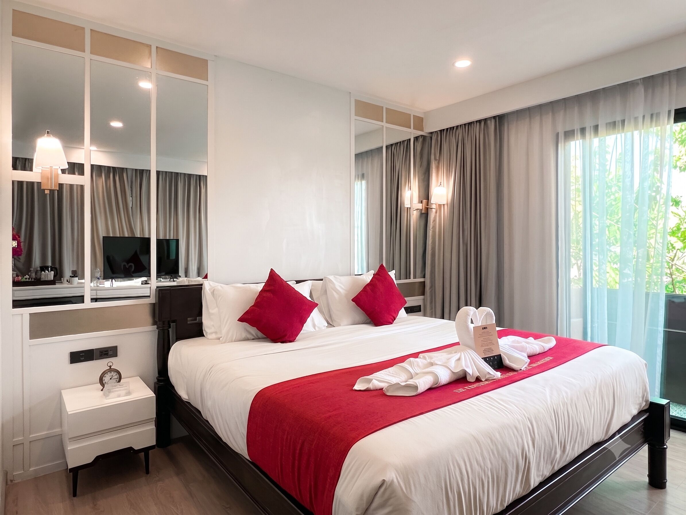 Une chambre d’hôtel avec un grand lit, une table de chevet, un miroir et une fenêtre avec des rideaux.