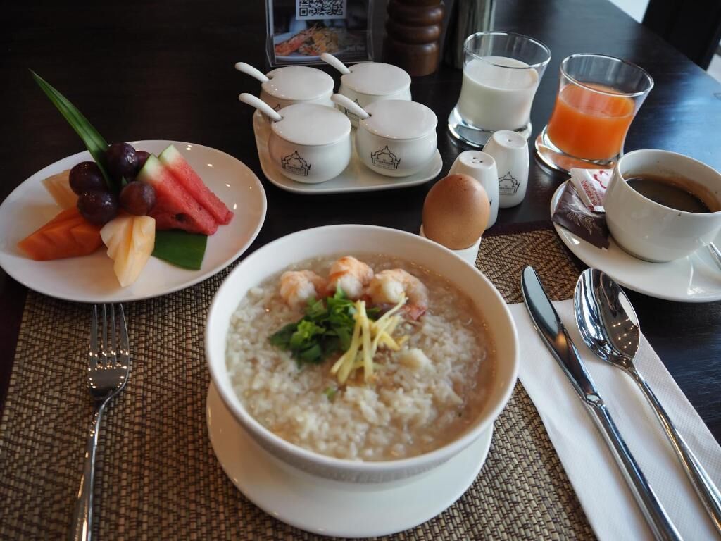 A breakfast setting with a bowl of oatmeal topped with shrimp and greens, a plate of fruit, and a cup of coffee.