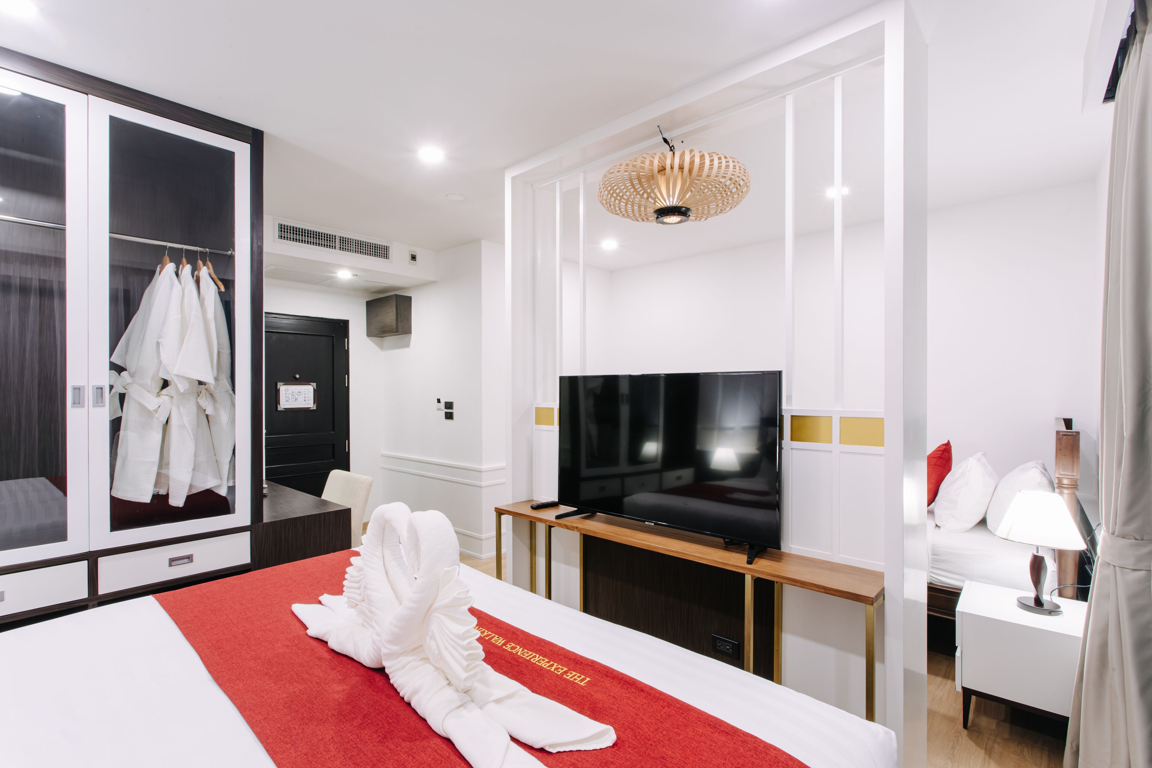 A hotel room with a large mirror, a flat-screen TV, a red carpet, a wooden side table, and a white bed.