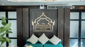 A reception area with a dark wood panel wall, a teal sofa with decorative pillows, and a sign reading "The Experience Walking Street Chiang Mai". - The Experience Walking Street Chiang Mai (Chiang Mai)