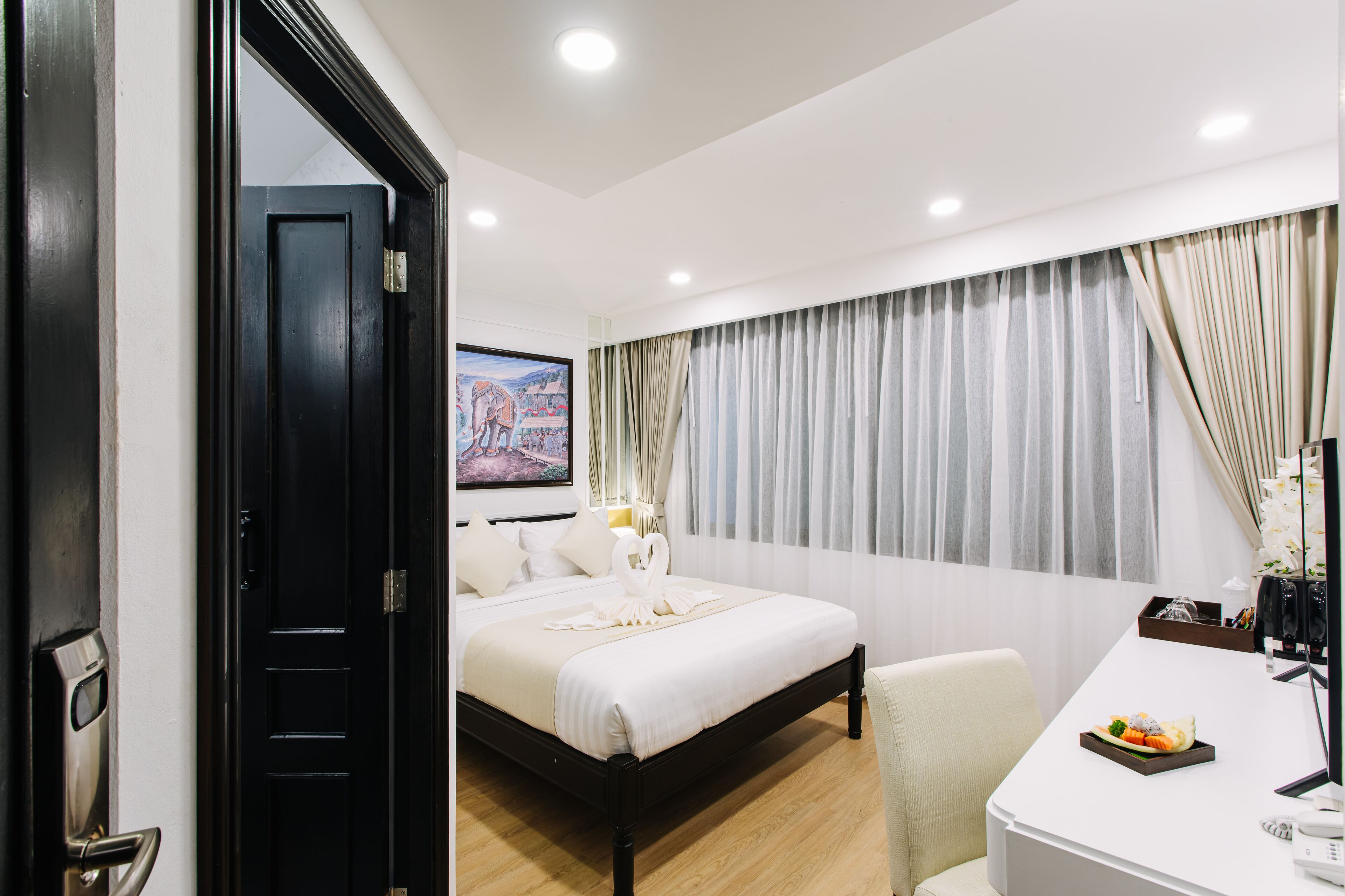 A hotel room with a bed, a desk, a chair, and a painting on the wall.