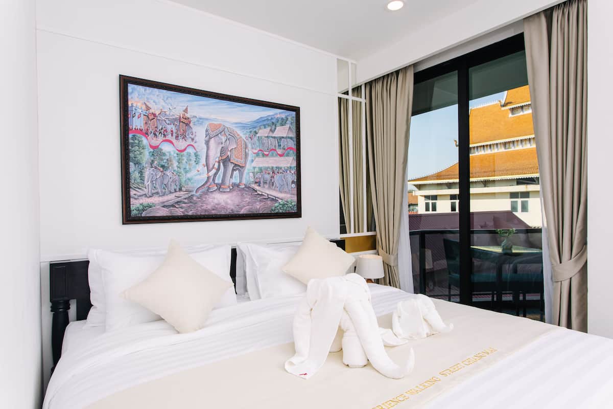 A hotel room with a large bed, a painting on the wall, and a view of a building through the window.