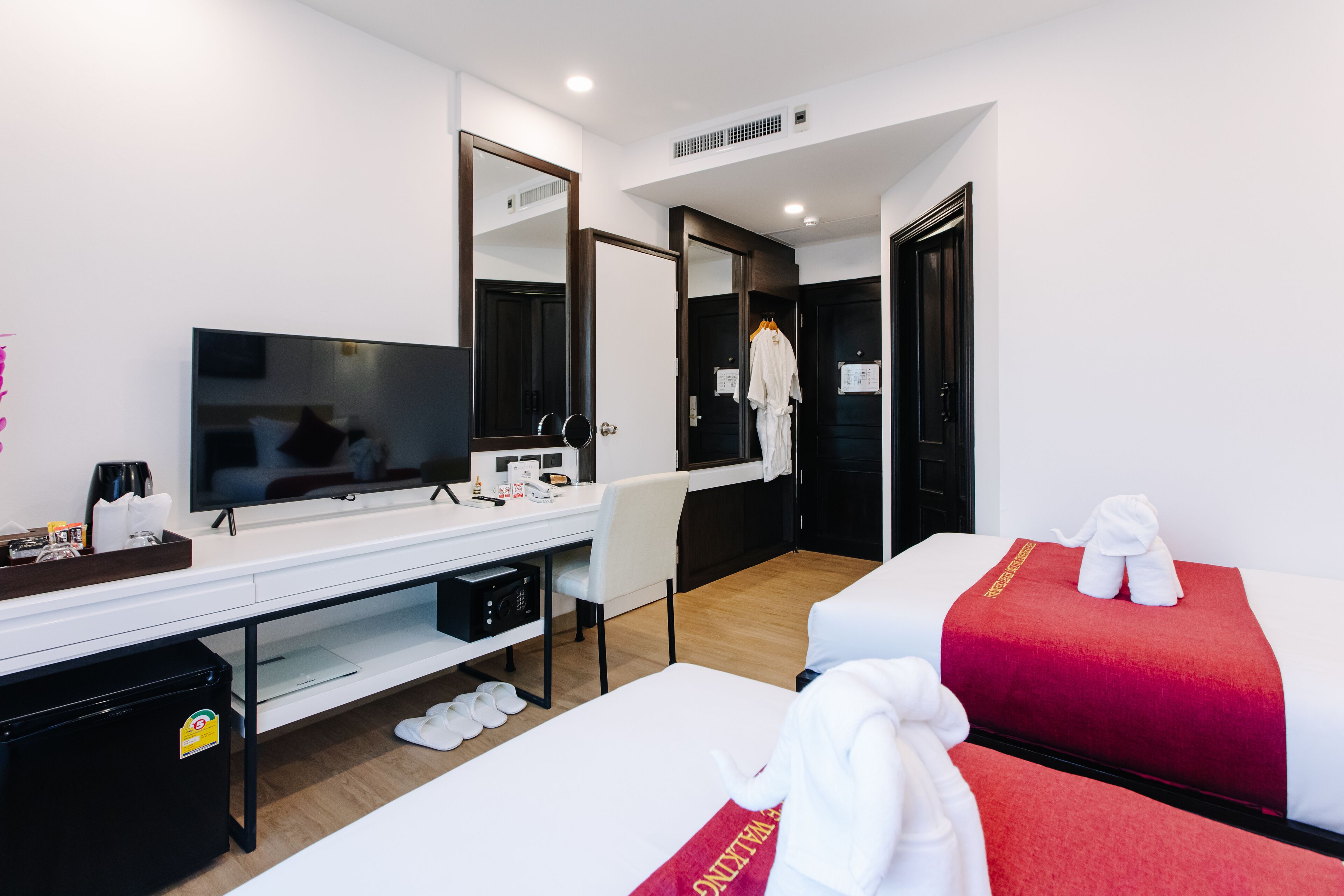 Une chambre d’hôtel avec un lit, un bureau avec une télévision, un miroir et un peignoir accroché à la porte.