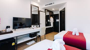 A hotel room with a bed, a desk with a TV, a mirror, and a robe hanging on the door.