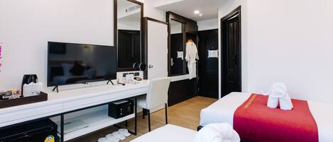 Een hotelkamer met een bed, een bureau met een televisie, een spiegel en een badjas die aan de deur hangt.