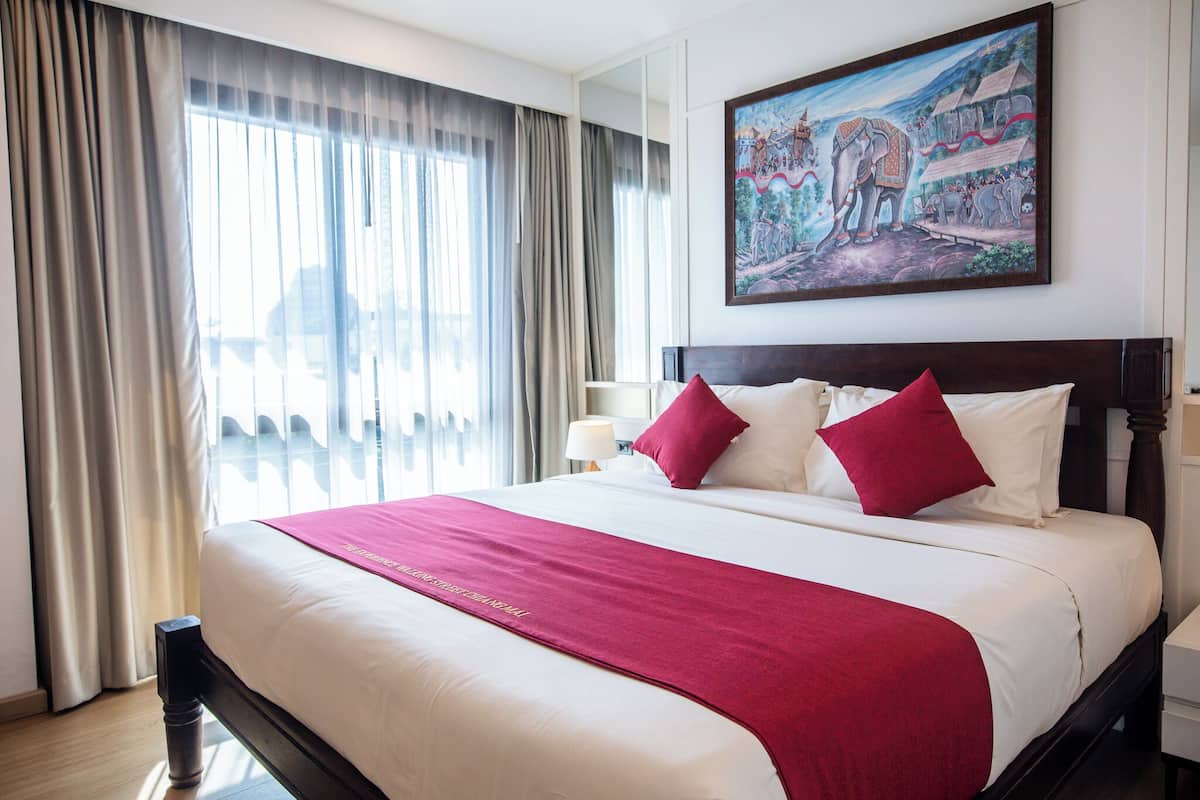 A hotel room with a large bed, a painting on the wall, and a window with curtains.