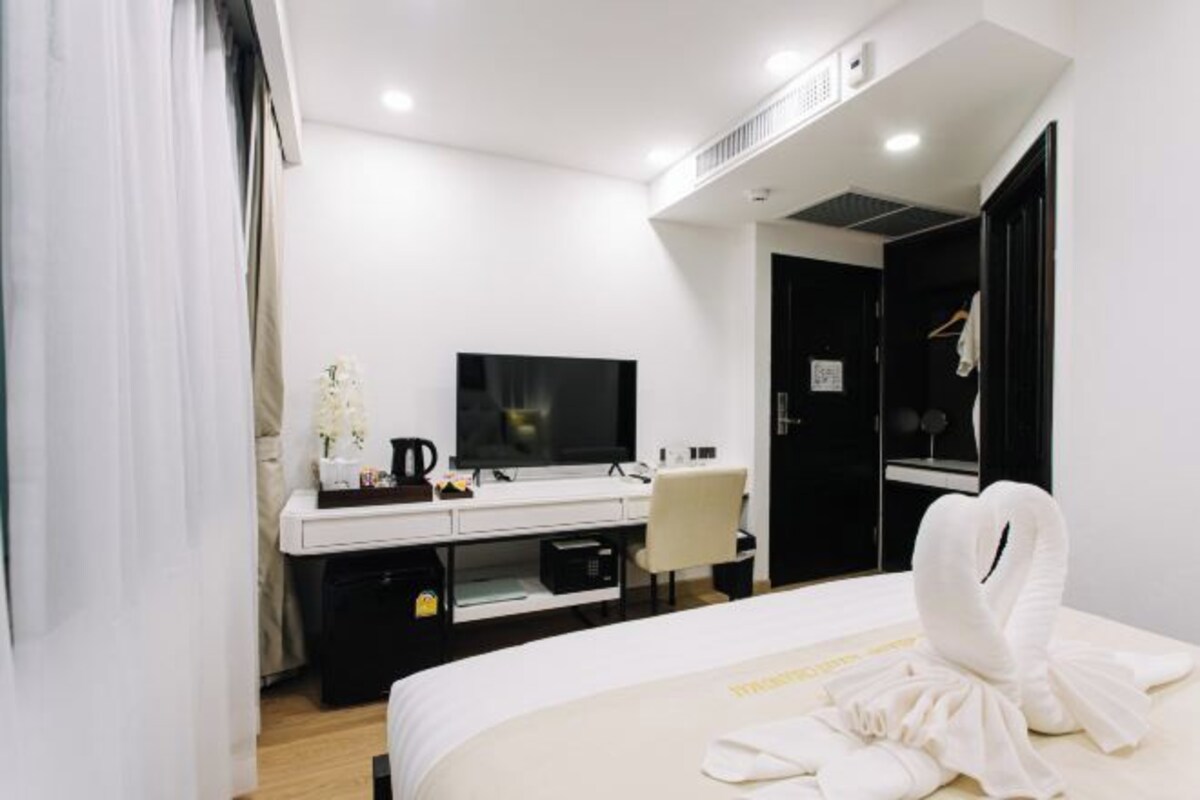 Una habitación de hotel moderna con una cama, un escritorio con televisor de pantalla plana, una silla y un armario.