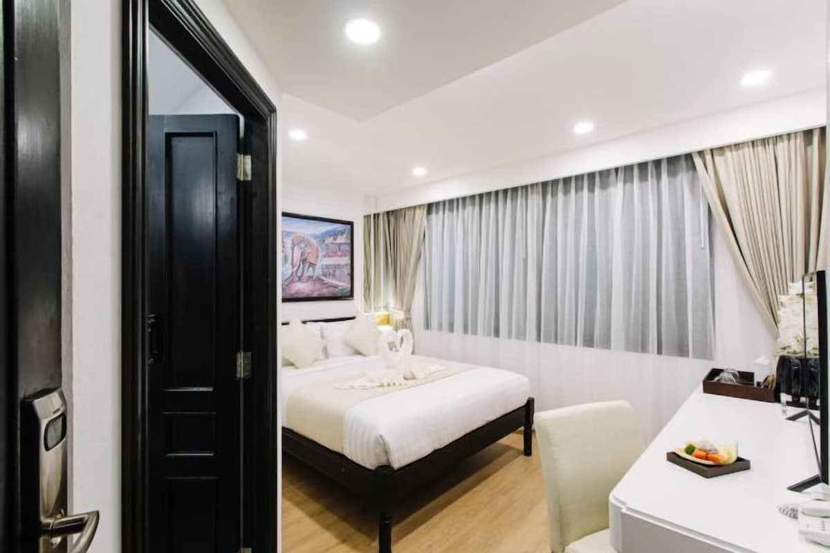 Habitación de hotel con cama, escritorio, silla, ventana con cortinas y un cuadro en la pared.