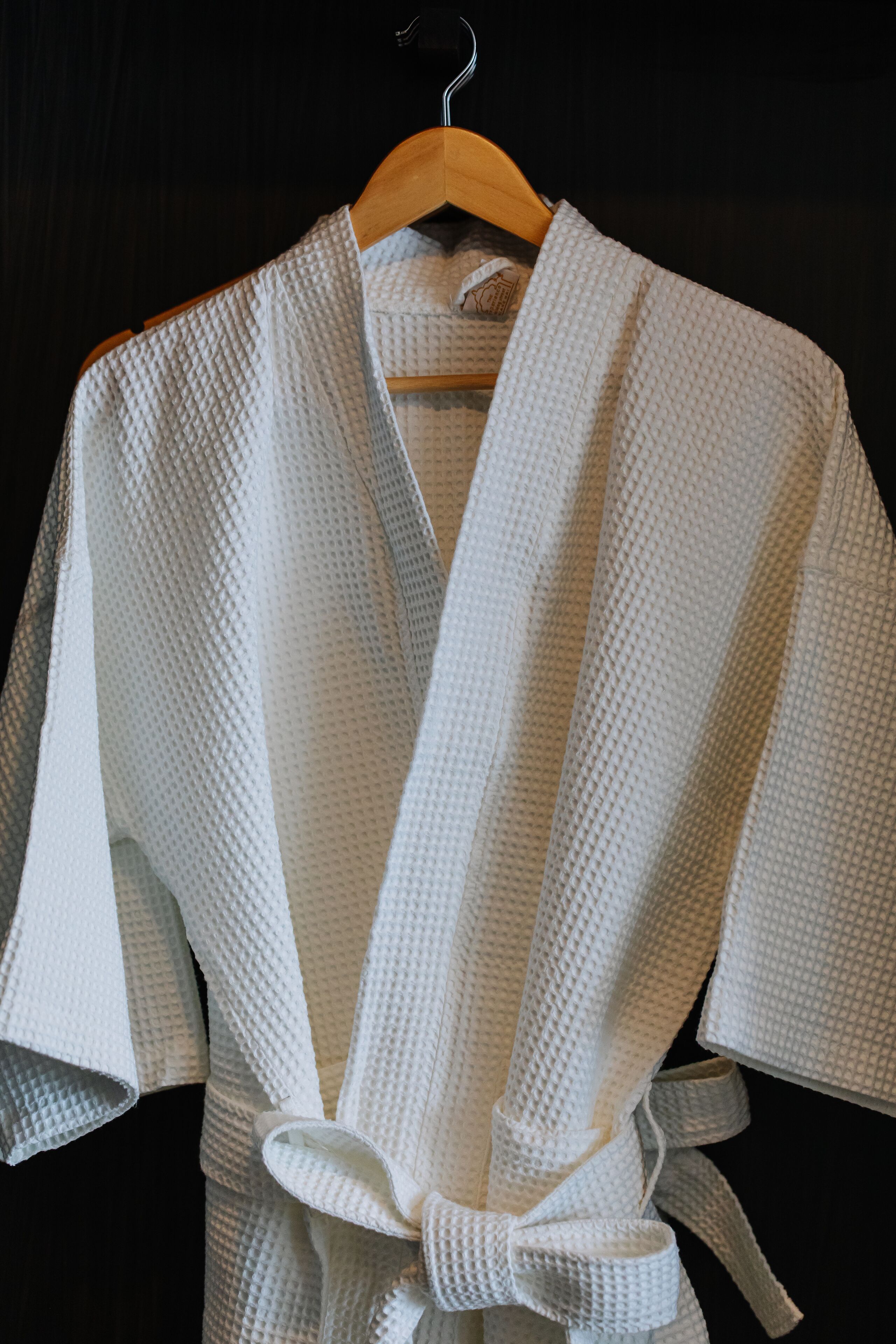 A white robe with a textured pattern, tied at the waist, hanging on a wooden hanger.
