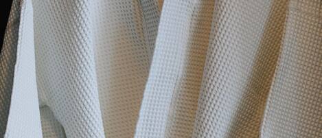 A white robe with a textured pattern, tied at the waist, hanging on a wooden hanger.