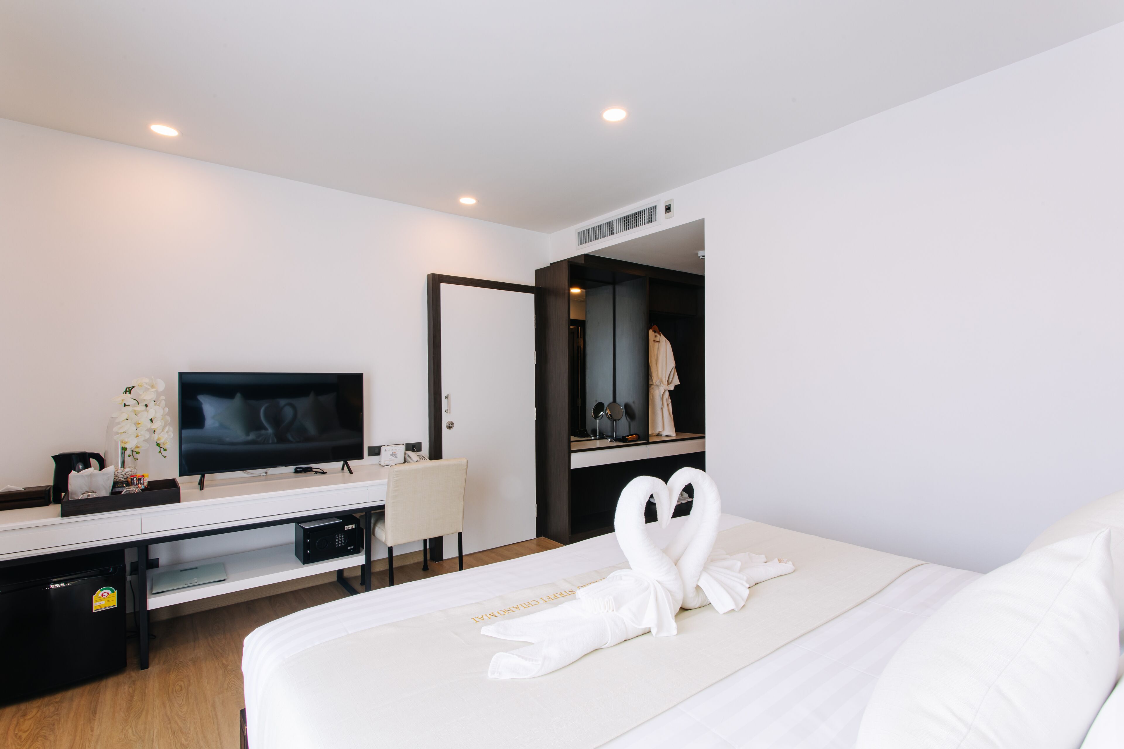 Ein modernes Hotelzimmer mit einem großen Bett, einem Fernseher, einem Schreibtisch mit Computer und einem Spiegel.