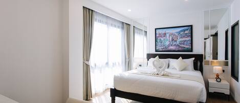 Una habitació d'hotel amb un llit gran, una cadira, un quadre a la paret i una tauleta de nit amb una làmpada.