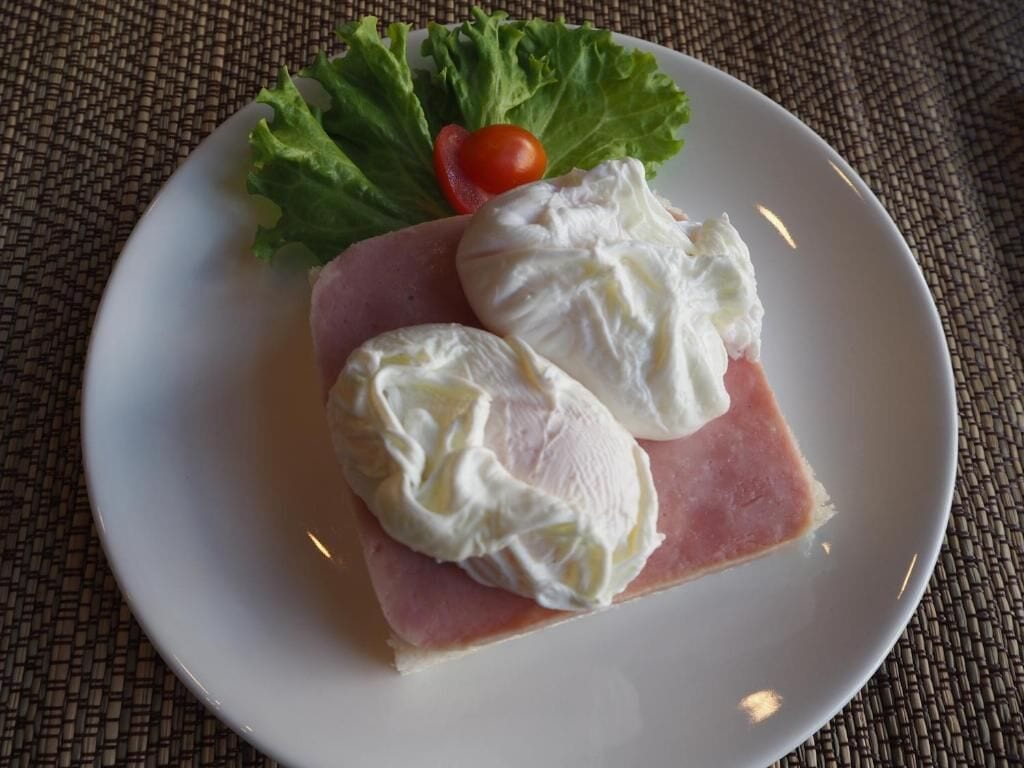 Une assiette blanche sur laquelle on voit une tranche de jambon et deux tranches de fromage, accompagnées d’une petite tomate et de quelques feuilles de laitue.