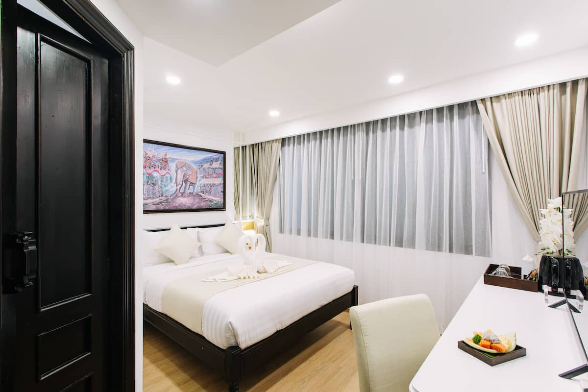 A hotel room with a bed, a desk, and a painting on the wall.
