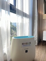 Ένα δωμάτιο με ένα μεγάλο παράθυρο, έναν λευκό καθαριστή αέρα και μια λευκή καρέκλα.
