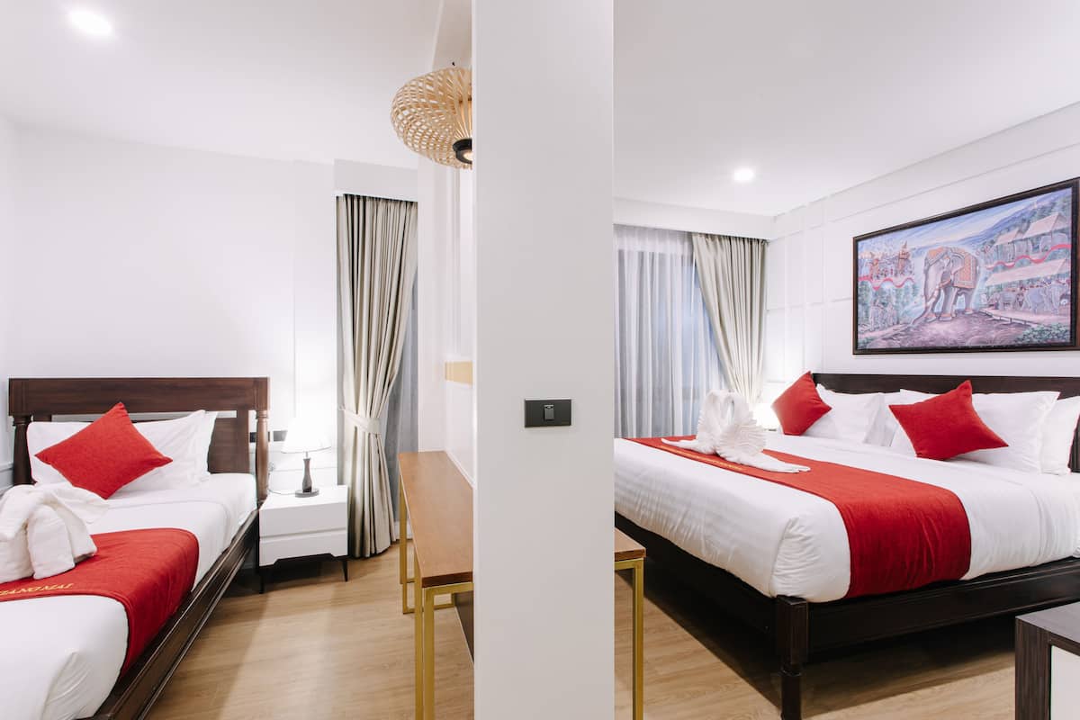 A hotel room with two beds, a wooden bench, a nightstand, a lamp, and a painting on the wall.