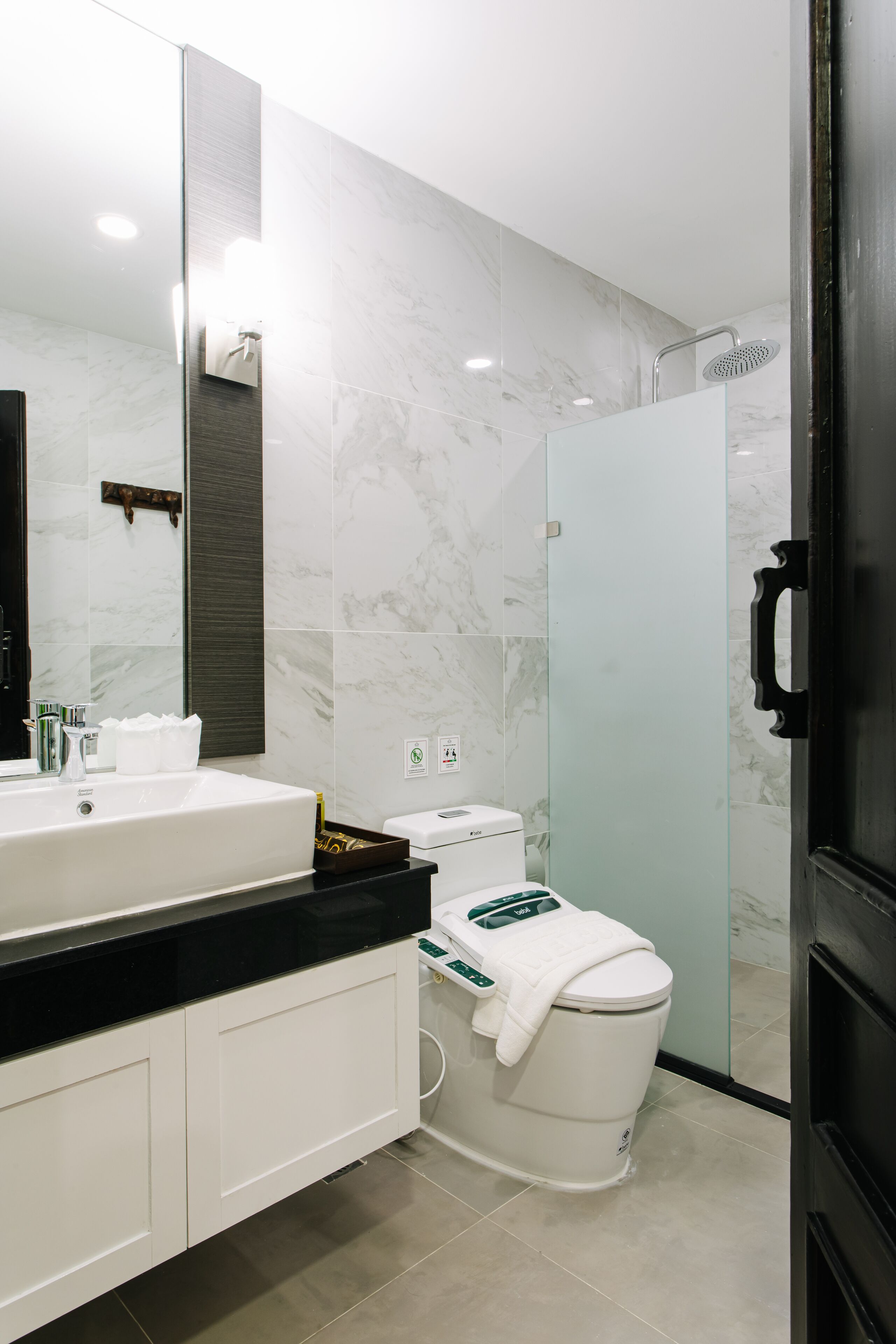 A modern bathroom with a large mirror, a white sink, a toilet, and a shower area.
