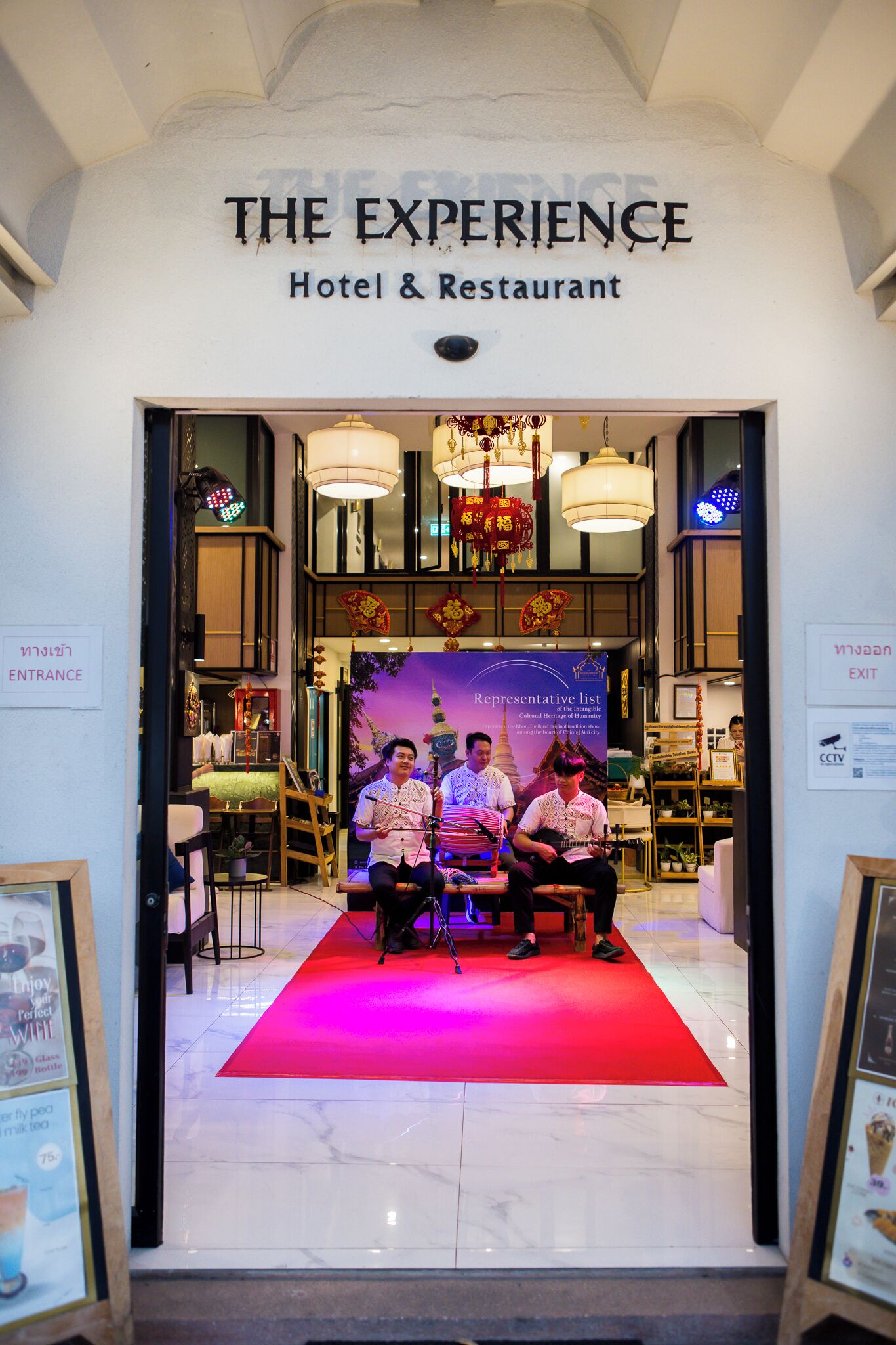The entrance of 'The Experience' hotel and restaurant with a red carpet, chandeliers, and a 'Representative list' banner.