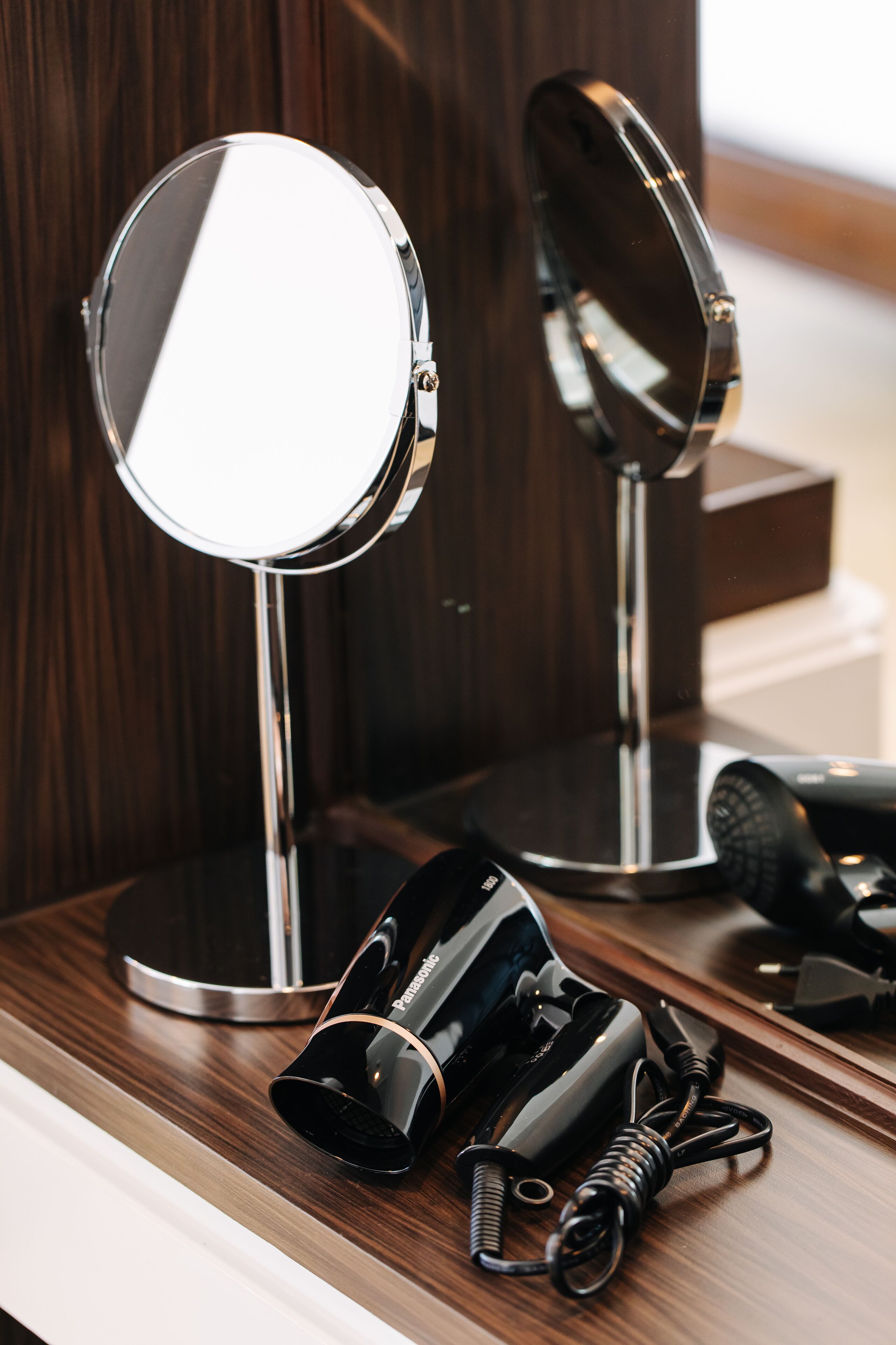 A bathroom vanity with a round mirror, a hairdryer, and a curling iron.