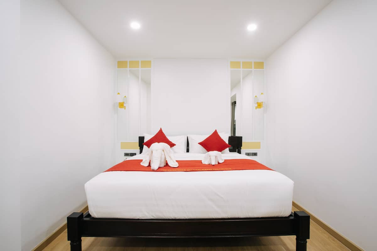 A neatly made bed with white linens and red pillows, a black headboard, and a wooden floor.