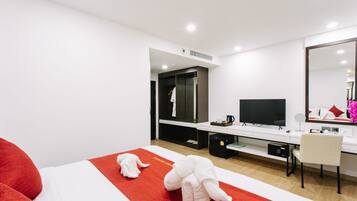Habitación de hotel con cama, escritorio, silla, televisor, espejo y armario.