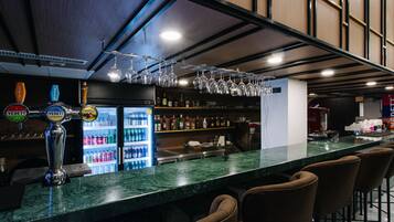 A bar area with a marble countertop, multiple beer taps, a refrigerator stocked with beverages, and bar stools.