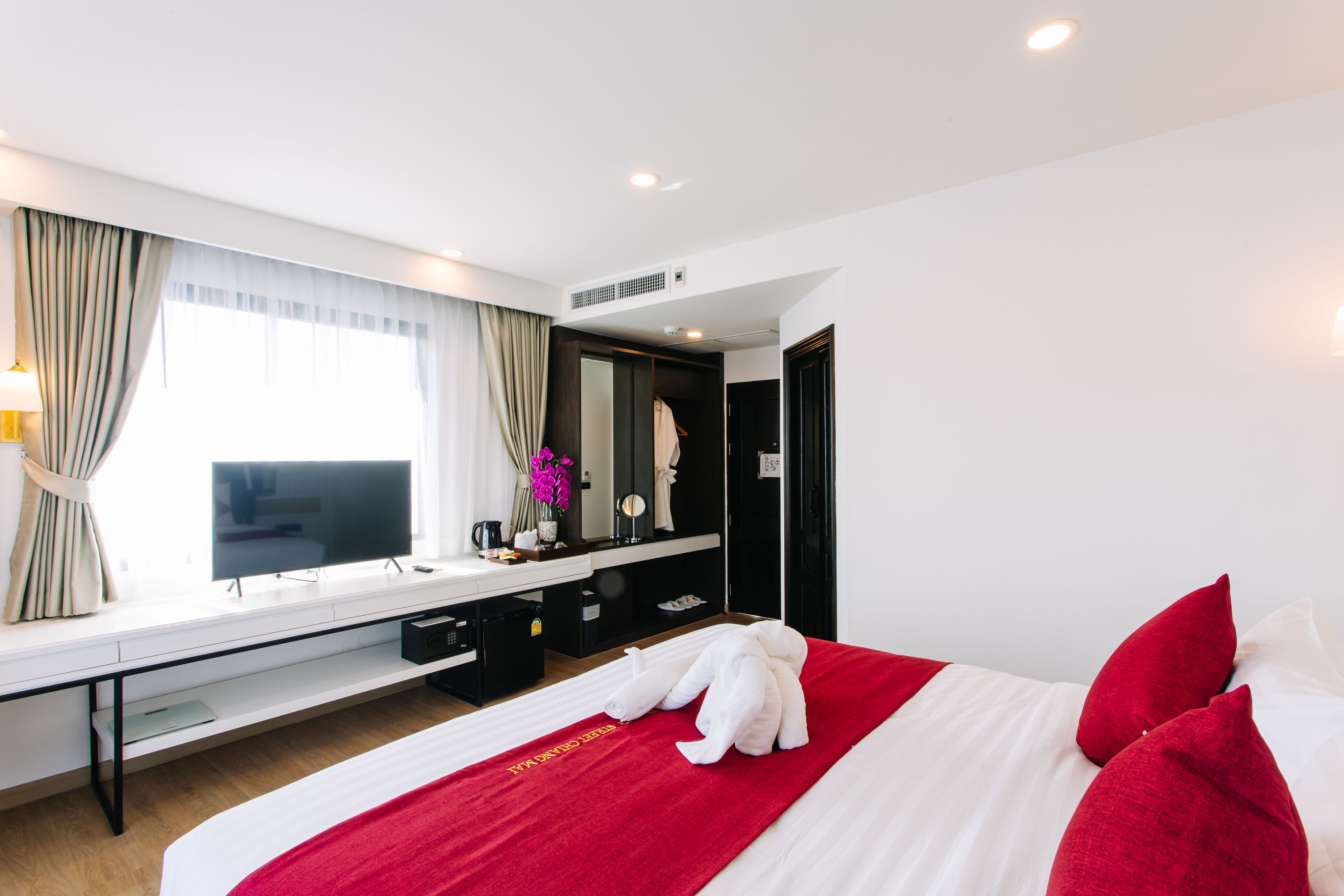 A hotel room with a large bed, a TV, a desk with a computer, and a mirror.