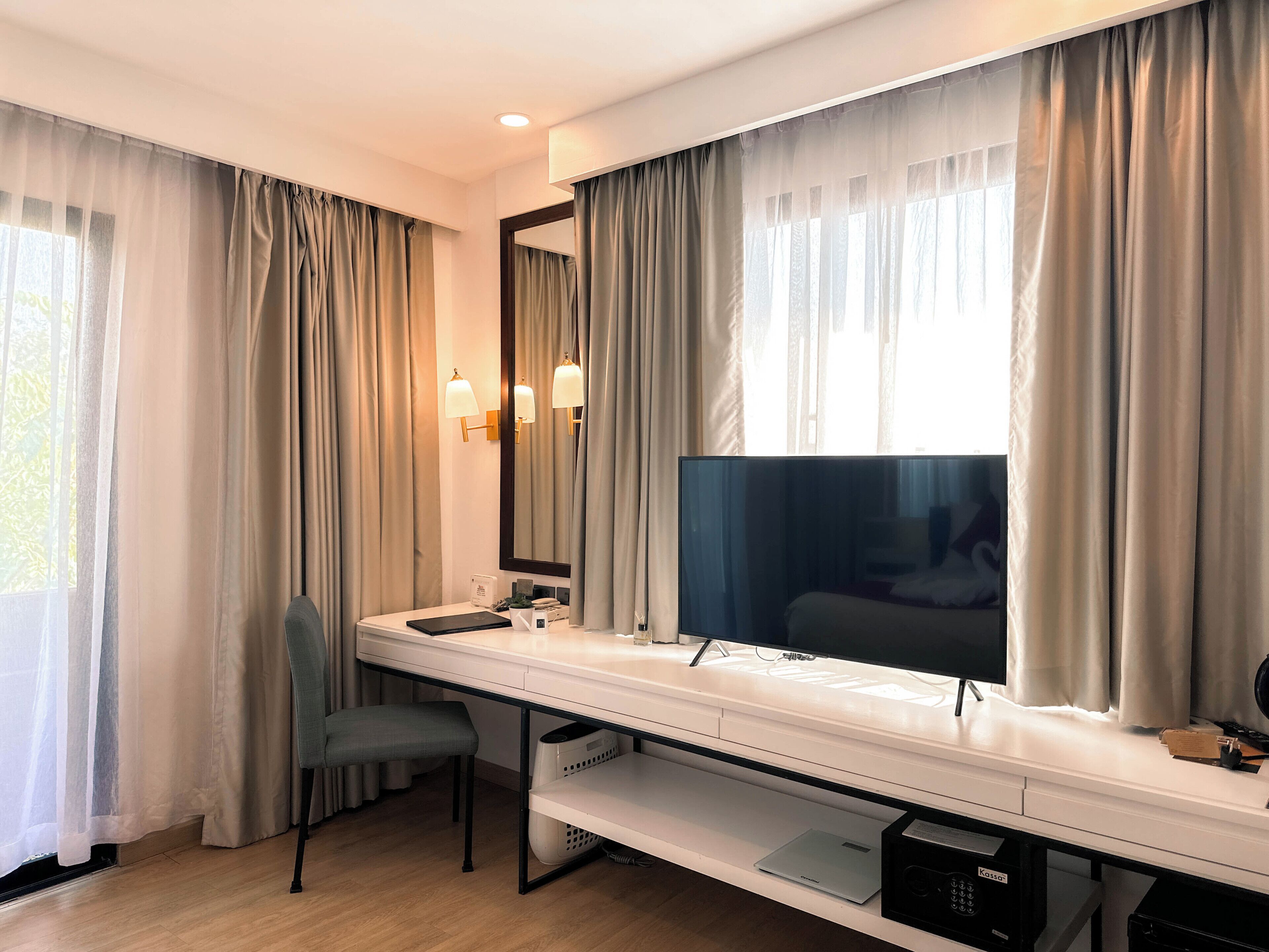 Et hotelværelse med seng, skrivebord med computer, stol, fjernsyn og gardiner.