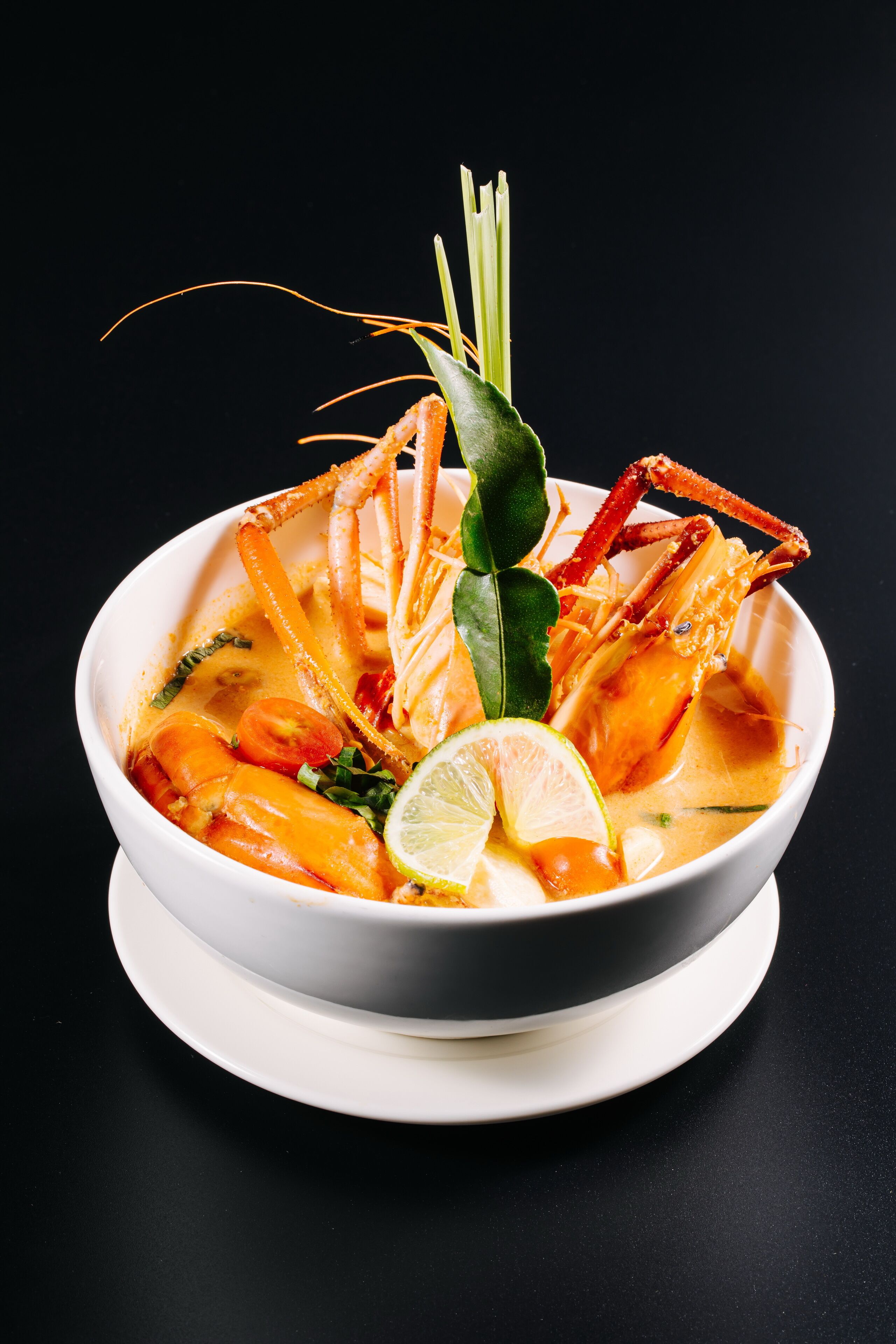 A bowl of seafood soup with a lime wedge and green garnish on a white plate.