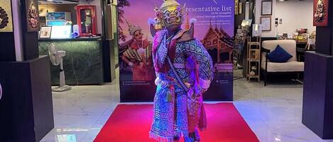 A person in traditional attire on a red carpet in a lobby with modern lighting and a backdrop displaying cultural heritage information.